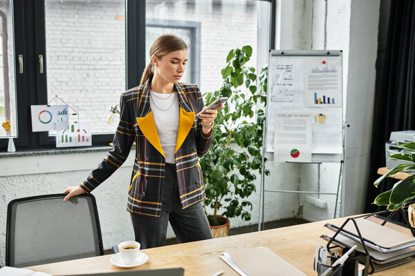 Молодой профессионал в шикарном клетчатом пиджаке фокусируется на своем смартфоне во время работы.