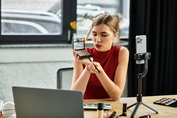 Привлекательная молодая фрилансер демонстрирует технику макияжа во время общения со своей аудиторией в Интернете.