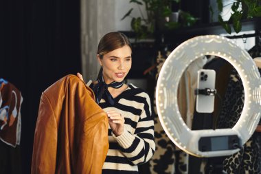 Genç nüfuzlu izleyicilere moda tavsiyeleri verirken, bir stüdyoda moda kıyafetlerini gösteriyor.