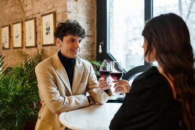 A joyful couple toasts with wine glasses, embracing their love at a cozy restaurant. clipart