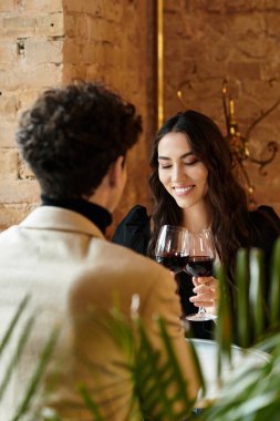 Young couple shares a joyful moment over red wine while celebrating their love in a restaurant. clipart