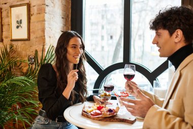 A happy couple enjoys a romantic meal with wine, celebrating their love in a cozy spot. clipart