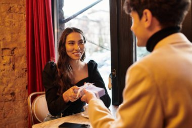 A couple exchanges thoughtful gifts, sharing smiles and love in a charming restaurant setting. clipart