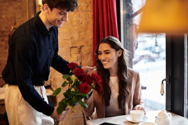 A young couple celebrates their love with roses and smiles at an intimate restaurant setting. clipart