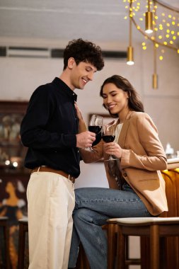 Genç bir çift şarap kadehlerini kaldırır, gülümserler ve romantik bir anın tadını çıkarırlar..