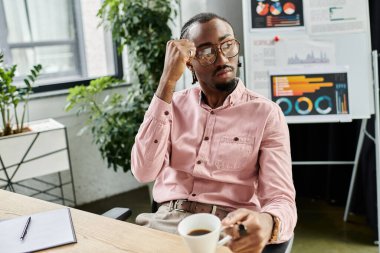 Genç bir Afrikalı Amerikalı, parlak bir ofiste kahve içerken derin düşünür..