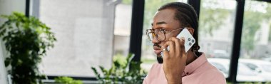 Odaklanmış genç adam cep telefonuyla iletişim kurarken kapalı bir alanda şık bir şekilde çalışıyor..