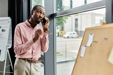 Genç bir Afrikalı Amerikalı adam telefonda konuşuyor, modern bir çalışma alanında derin düşünceler içinde..