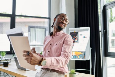 Genç bir Afrikalı Amerikalı, modern ofis ortamında çalışırken gülümsüyor..