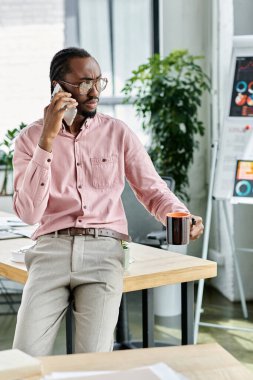 Genç bir Afrikalı Amerikalı, modern bir çalışma alanında kahve yudumlarken bir telefon görüşmesi yaptı..