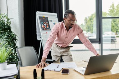 A young african american man in a pink shirt is immersed in his work at a stylish desk. clipart