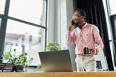 Şık bir genç adam, canlı bir çalışma alanında bitkilerle kahve yudumlarken telefonda konuşuyor..