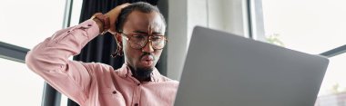 A young african american man concentrates on his laptop screen, revealing surprise and concern. clipart