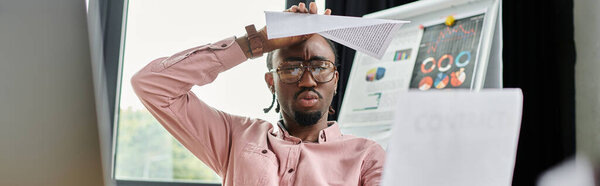 Young African American man struggles with focus while working remotely in a stylish workspace.