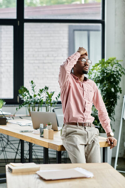 Young man pauses at his desk in a chic coworking space, reflecting on his projects.