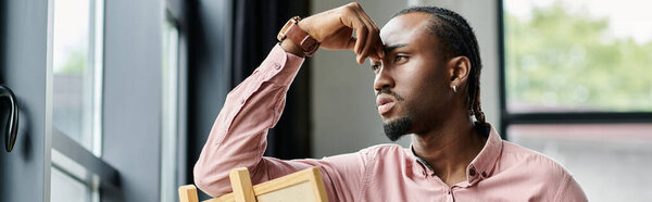 A thoughtful young man contemplates his future while seated at a window desk.