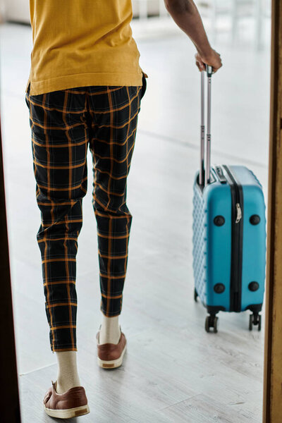 Молодой афроамериканец вытаскивает чемодан, готовый принять свой удаленный трудовой образ жизни.