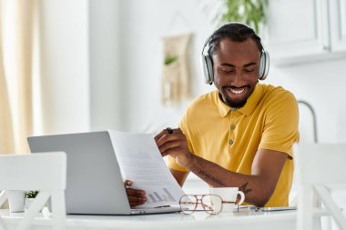Genç bir Afrikalı Amerikalı adam, uzaktan çalışan belgelerle ve dizüstü bilgisayarla gülümsüyor..