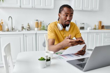 A focused young man engages in remote work, surrounded by a bright kitchen setup. clipart