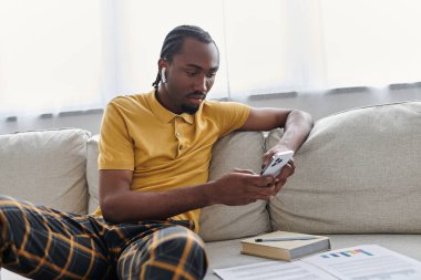 Genç bir adam akıllı telefonuyla meşgul oluyor, evde dinlenirken işine odaklanıyor..