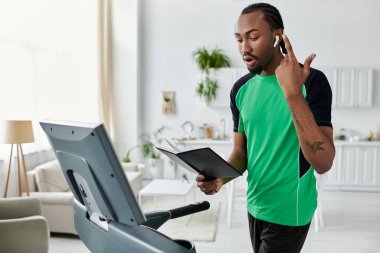 A young african american man multitasks on an exercise machine while attending to work tasks. clipart