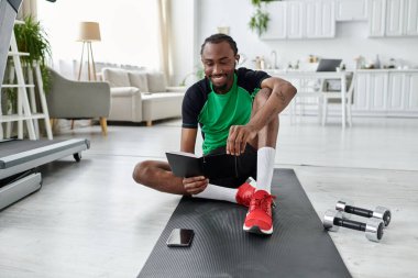 Yakışıklı genç bir adam spor paspasının üzerinde rahatlıyor, şık bir evde tabletine odaklanıyor..