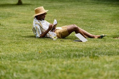 Genç bir adam yemyeşil bir parkta otların üzerinde uzanırken huzurlu bir çalışma seansının keyfini çıkarıyor..