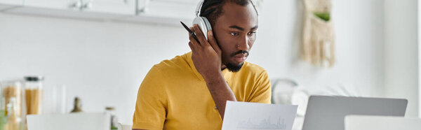 Красивый молодой человек занимается отдаленной работой из своего хорошо освещенного домашнего офиса, демонстрируя кочевую жизнь.