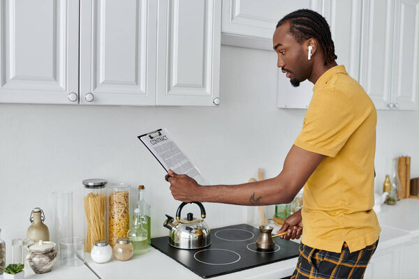 A focused young man follows a recipe while boiling water to make tea in a sleek kitchen.