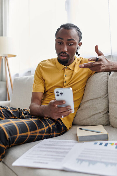 Сосредоточенный молодой человек взаимодействует со своим смартфоном, сидя в стильном жилом пространстве.