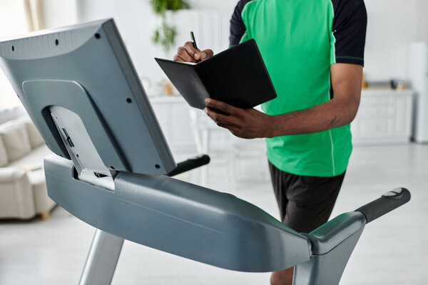 Сосредоточенный молодой человек делает заметки во время занятий на беговой дорожке в стильном помещении.