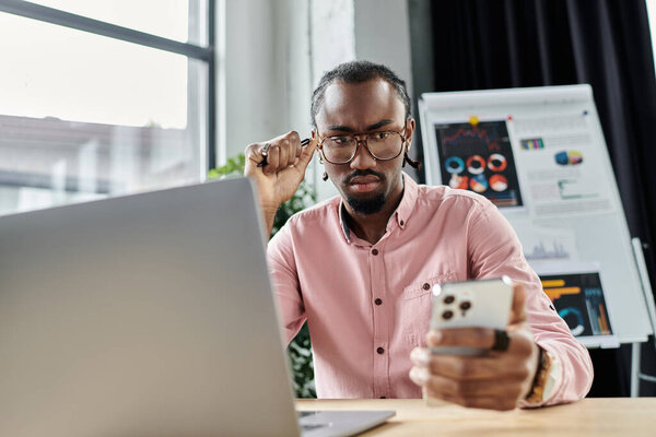 Сосредоточенный молодой человек рассматривает информацию на своем смартфоне, сидя за гладким столом.