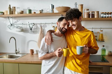 İki adam şık mutfaklarında neşeli bir anı paylaşıyor, bol bol gülümseme ve sıcaklık..