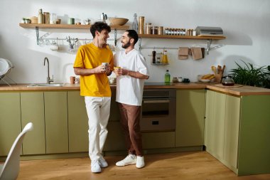 Gündelik giysiler içindeki iki adam, şık mutfaklarında birlikte vakit geçirmenin keyfini çıkarıyorlar, aşk saçıyorlar..