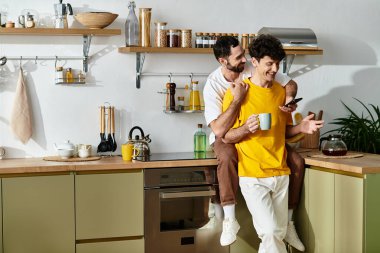 İki erkek, şık mutfaklarında birbirlerine eşlik ederek ve kahkaha atarak hassas bir anı paylaşıyor..