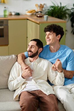 In a modern apartment, two men enjoy each others company while smiling and holding hands. clipart