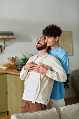 İki adam birlikte hassas bir anı paylaşıyor, şık bir dairede eğleniyorlar..