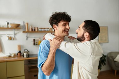 İki adam şık evlerinde, sevgi ve mutlulukla kucaklaşarak neşeli bir anı paylaşıyor..