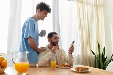 İki adam rahat evlerinde kahvaltıdan zevk alır, gülümsemelerini ve yemeklerini paylaşırlar..