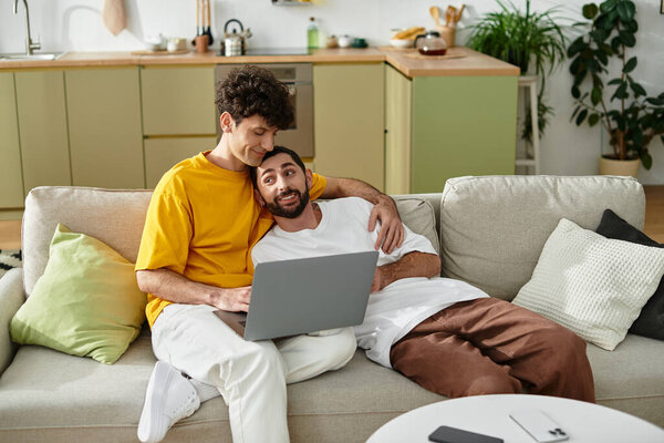 Двое мужчин наслаждаются уютным моментом на диване в своей стильной квартире, обнимая любовь.