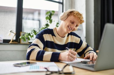 A young man in a striped sweater smiles as he works in a modern office. clipart