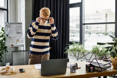 Çizgili kazaklı genç kızıl adam aktif olarak laptopuyla şık bir ofis ortamında takılıyor..