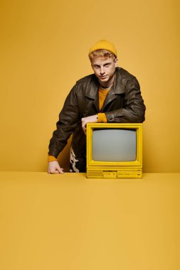 Tarz sahibi genç kızıl, modaya uygun kış kıyafetleri içinde eski bir televizyona yaslanarak poz veriyor.