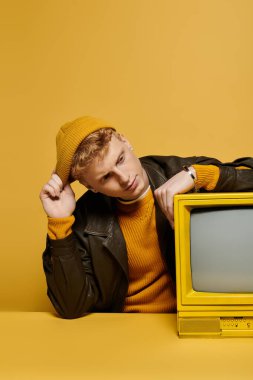 Kırmızı saçlı şık bir genç adam, sarı bir arka plana karşı kış kıyafetiyle rahatlar..