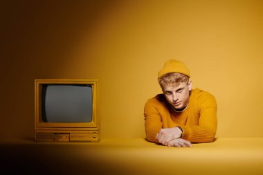 A young redhead shows off his stylish winter outfit near vintage television against a bright yellow background. clipart