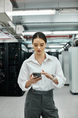 Yüksek teknolojili sunucu odasında dikilirken beyaz gömlekli bir bilişim uzmanı sistemleri izliyor..