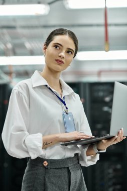 Beyaz gömlekli yetenekli bir kadın yüksek teknolojili sunucu odasında çalışıyor ve ağ sistemlerini yönetiyor..