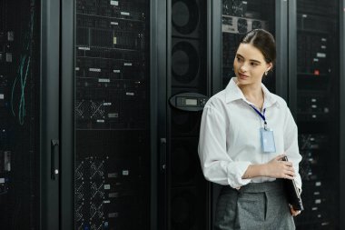 Beyaz gömlekli profesyonel bir kadın modern bir teknoloji tesisindeki sunucu sistemlerini izliyor..