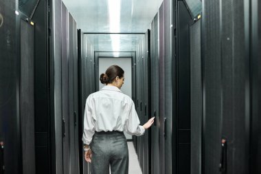 Professional woman in a white shirt works diligently among server racks in a data center. clipart