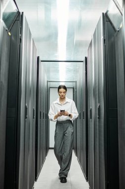 A professional woman in a white shirt works with a mobile device in a data center. clipart